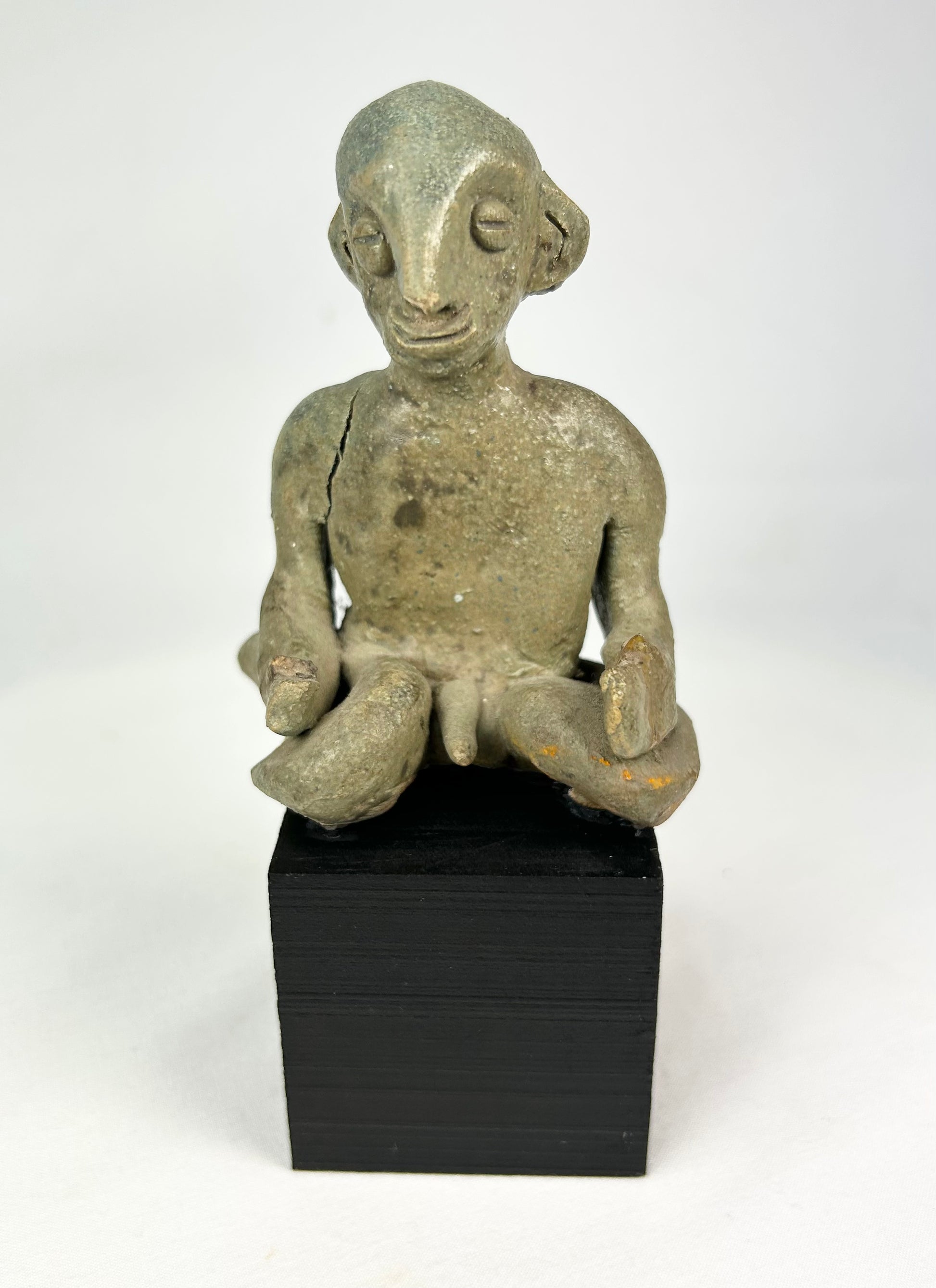 Hand-modeled West Mexican Nayarit Chinesco terracotta figure of a seated male with slit eyes, pinched nose, cross-legged pose, and red/orange pigment remnants, featuring earthen and mineral accretions, mounted on a modern wood display block, ca. 100 BCE–300 CE