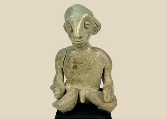 Hand-modeled West Mexican Nayarit Chinesco terracotta figure of a seated male with slit eyes, pinched nose, cross-legged pose, and red/orange pigment remnants, featuring earthen and mineral accretions, mounted on a modern wood display block, ca. 100 BCE–300 CE