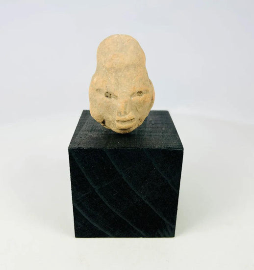 Small Pre-Columbian terracotta head fragment from West Mexico shaft-tomb culture, circa 300 BCE–300 CE, with almond-shaped eyes, defined features, and elongated cranial form, mounted on a black display base, photographed on a white background.