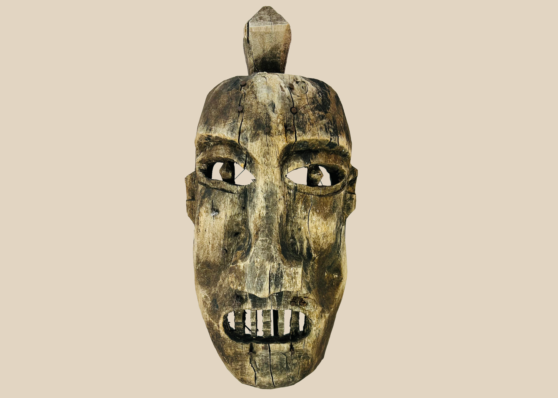 Front view of an aged wooden ritual mask displayed on a museum-style stand against a white background.
