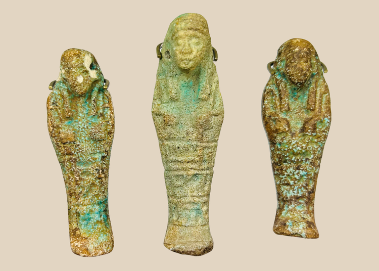 Three ancient Egyptian faience ushabti figures with turquoise and earthen patina displayed on a beige background.