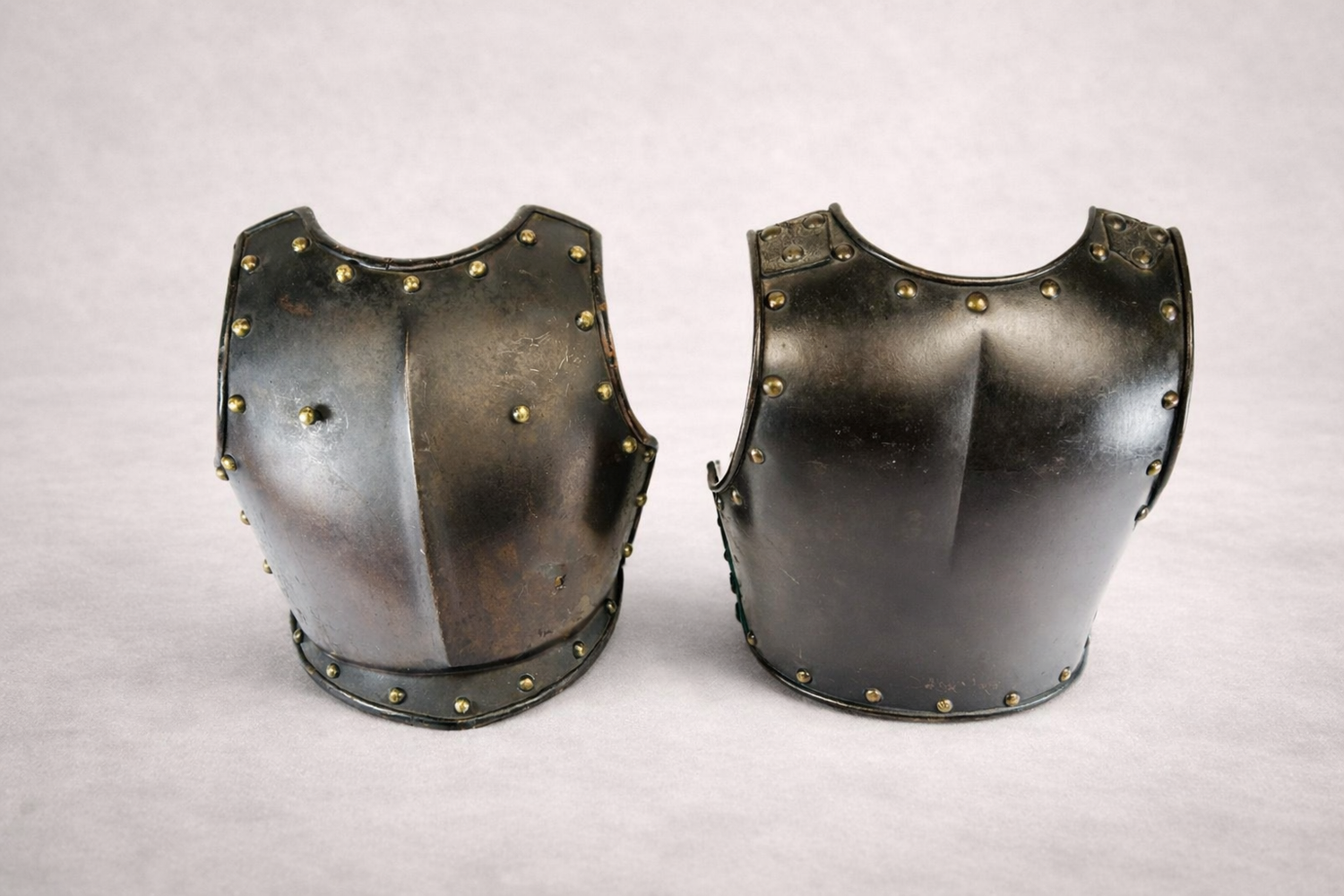 Pair of antique steel breastplates with riveted edging, 19th century European armor display on neutral background