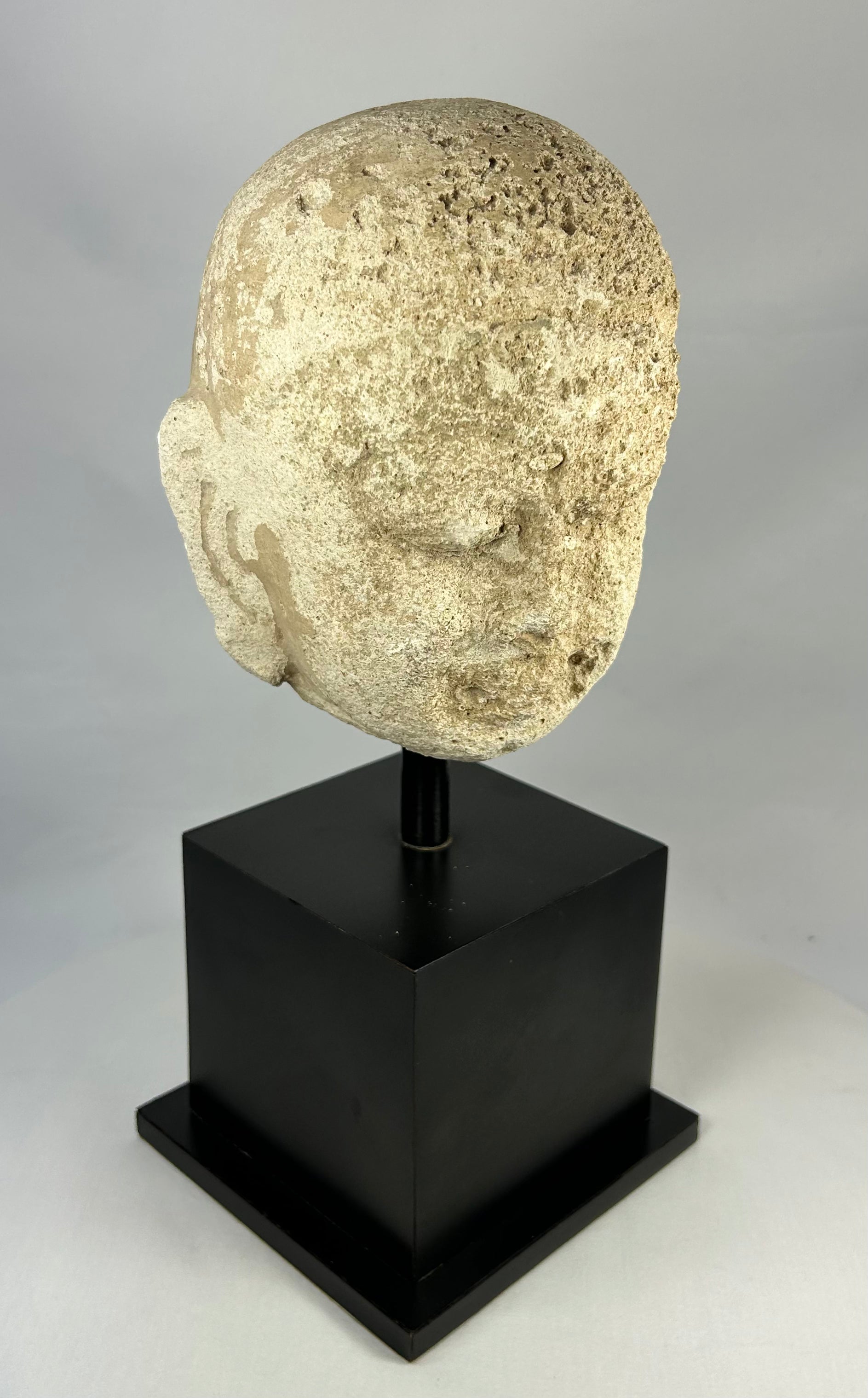 Southeast Asian carved stone Buddha head with serene expression and closed eyes, 13th–14th century, mounted on a modern black stand, Burma or Thailand.