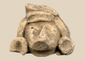 Pre-Columbian carved stone head fragment with recessed eyes, triangular nose, and circular earspools