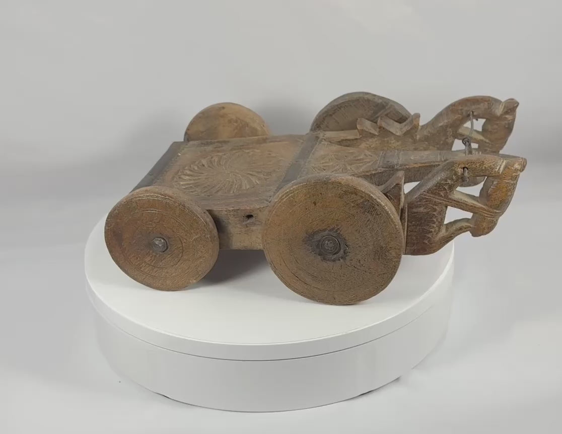 360-degree rotating view of an antique South Asian carved wooden ceremonial cart featuring stylized animal-head terminals, geometric chip-carved decoration, original iron elements, and four solid wooden wheels with a rich historic patina.