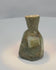 Rotating view of an ancient Roman blown green glass unguentarium with a compact body, thick cylindrical neck, narrow opening, flattened base, heavy iridescence, mineral deposits, and burial weathering