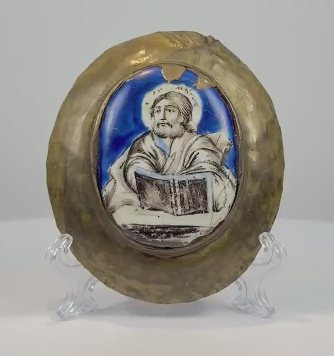 180-degree rotating view of an antique 18th–19th century Russian Orthodox enamel icon plaque depicting a bearded, haloed saint holding a Gospel book. The hand-painted icon features a vibrant cobalt-blue background, Cyrillic inscription, and an aged oval bronze frame, revealing its curved profile and natural patina.