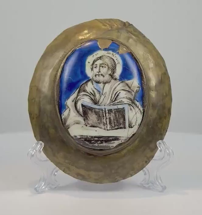 180-degree rotating view of an antique 18th–19th century Russian Orthodox enamel icon plaque depicting a bearded, haloed saint holding a Gospel book. The hand-painted icon features a vibrant cobalt-blue background, Cyrillic inscription, and an aged oval bronze frame, revealing its curved profile and natural patina.