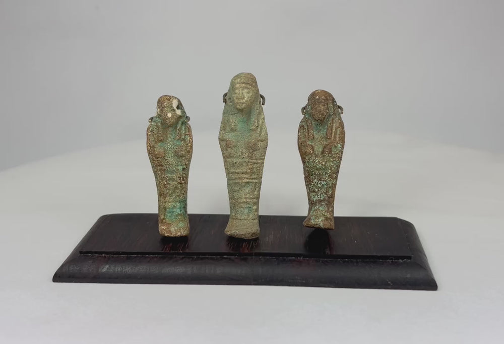 Trio of ancient Egyptian faience ushabti figures mounted on a dark hardwood base against a white studio background.