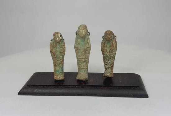 Trio of ancient Egyptian faience ushabti figures mounted on a dark hardwood base against a white studio background.