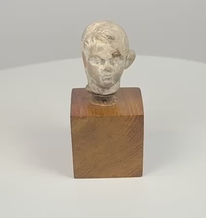 Video of an ancient terracotta head fragment on a wooden base, showing youthful facial features, sculpted hair, and a weathered surface.