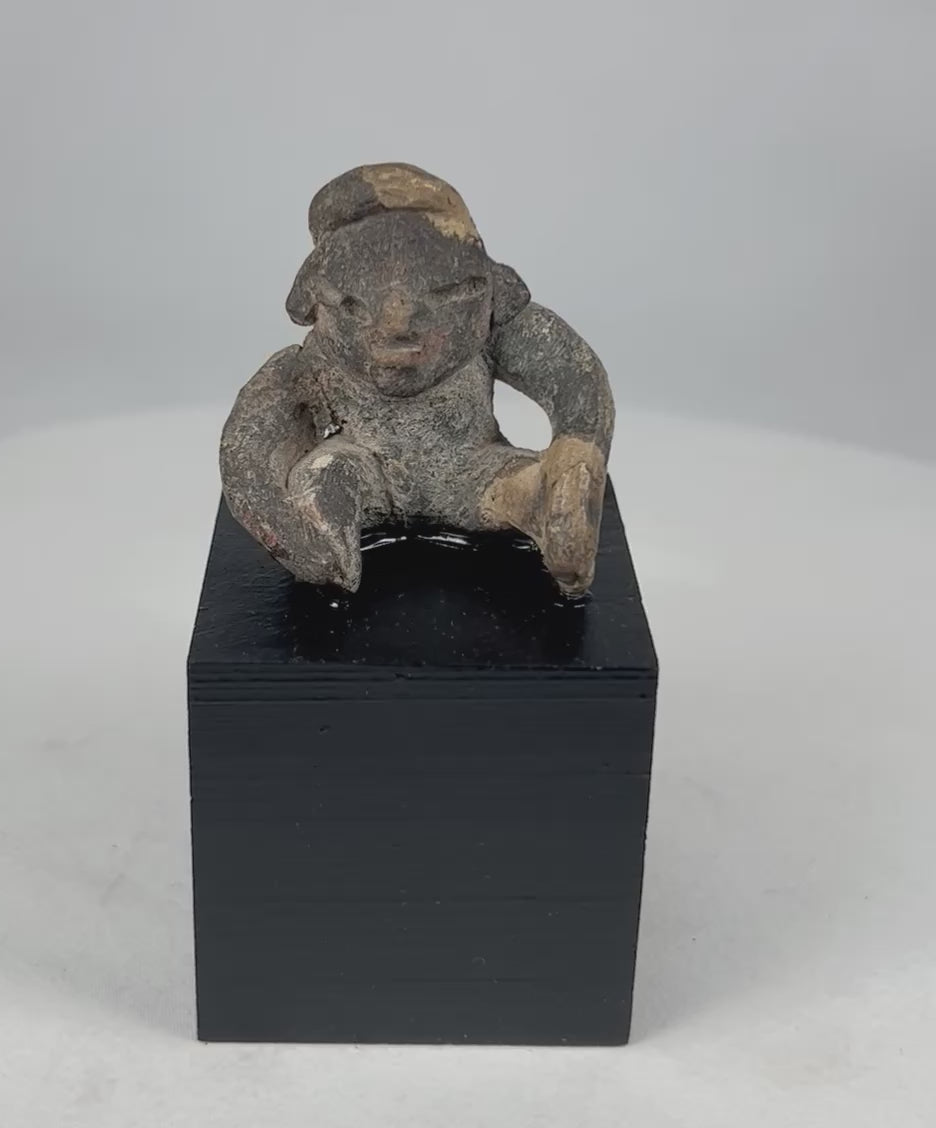 360-degree video of an ancient Pre-Columbian West Mexican seated terracotta figure showing full form, stylized facial features, surface encrustation, and archaeological patina