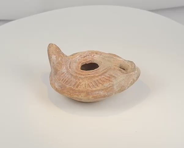 Rotating view of a Late Roman to Early Byzantine mold-made terracotta oil lamp with a central filling aperture, separate wick opening, raised nozzle channel, radiating decoration, solid rear handle, concentric base rings, and burial encrustation
