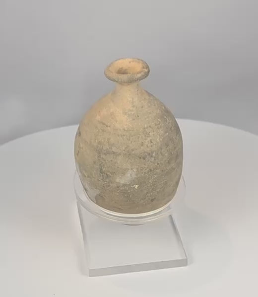 Rotating view of an ancient Roman to Byzantine terracotta bottle with a compact ovoid body, gently sloping shoulders, short constricted neck, broad thickened everted rim, narrow opening, subtle wheel-turning lines, pale buff surface, mineral deposits, burial accretions, surface weathering, and a custom clear acrylic display stand
