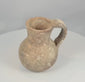 Rotating view of an ancient Roman to Byzantine terracotta pouring jug with a compact globular body, tall narrowing neck, outward-flaring rim, pinched pouring mouth, substantial loop handle, small circular base projection, reddish-brown clay fabric, pale mineral deposits, burial encrustation, rim wear, and archaeological patina