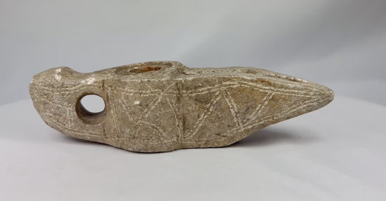 360-degree rotating video of a medieval Islamic carved stone oil lamp, showing its deep oil chamber, elongated wick channel, loop handle, and aged patinated surface.