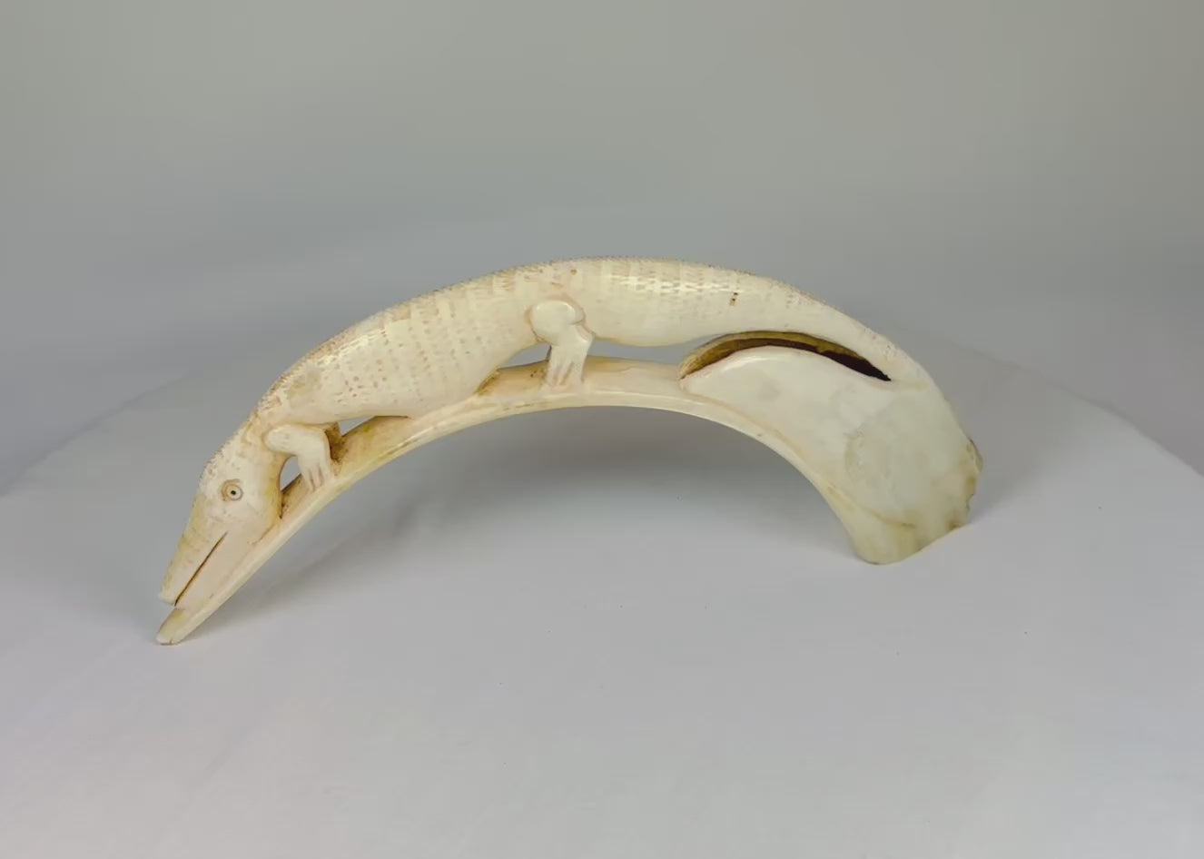 Hand-carved African hippopotamus incisor tusk featuring an intricately detailed crocodile in high relief along the natural curvature, polished with rich patina, displayed on a white background.