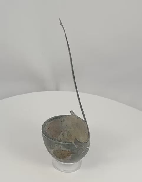 Rotating view of an ancient Roman bronze simpulum ladle with a deep hemispherical bowl, long flat-section curved handle, broad triangular attachment, two raised spur-like projections, incomplete upper terminal, dark blue-green patina, mineral accretions, corrosion, cracks, perforations, edge losses, and archaeological surface wear