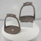 Rotating view of a pair of antique Chinese hand-forged iron stirrups with broad pierced footplates, suspension loops, decorative chiseled details, and aged patina