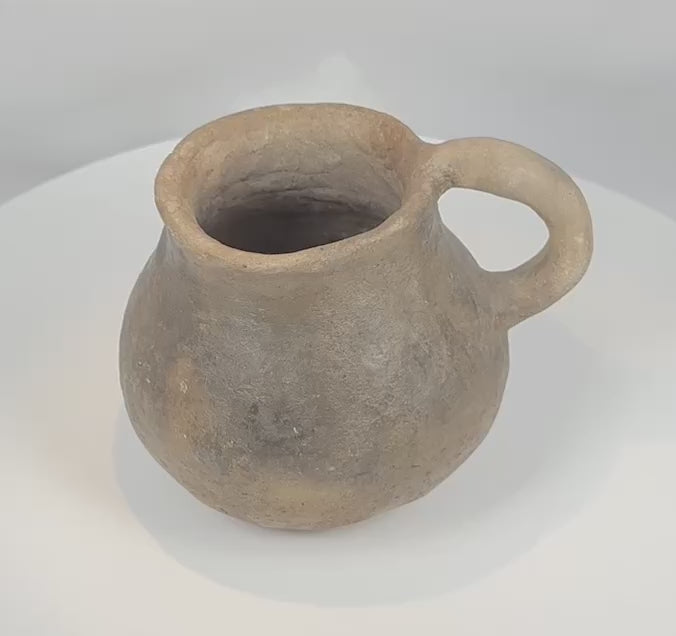 Rotating view of an authentic Pre-Columbian Casas Grandes pottery mug from northern Mexico, highlighting its hand-formed earthenware construction, globular body, flared rim, curved strap handle, archaeological patina, and centuries-old Paquimé craftsmanship.