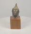 360-degree video of a Thai bronze Buddha head on a wooden base, showing textured curls, a pointed topknot, and elongated earlobes.