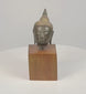 360-degree video of a Thai bronze Buddha head on a wooden base, showing textured curls, a pointed topknot, and elongated earlobes.