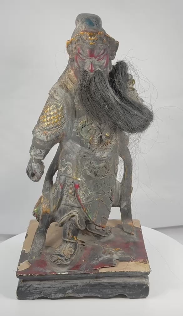 Rotating view of an antique Chinese carved wood statue of Guan Yu with a red-painted face, long natural-fibre or horsehair beard, elaborate polychrome armour, gilt details, dragon decoration, missing weapon, and integral base