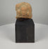 Ancient Gandharan terracotta relief plaque fragment from the 2nd–4th century CE, featuring a weathered central male bust with almond-shaped eyes, a rounded hairstyle or headdress, faint attendant figures, reddish-brown clay, natural encrustation, and a custom display base.