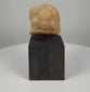 Ancient Gandharan terracotta relief plaque fragment from the 2nd–4th century CE, featuring a weathered central male bust with almond-shaped eyes, a rounded hairstyle or headdress, faint attendant figures, reddish-brown clay, natural encrustation, and a custom display base.