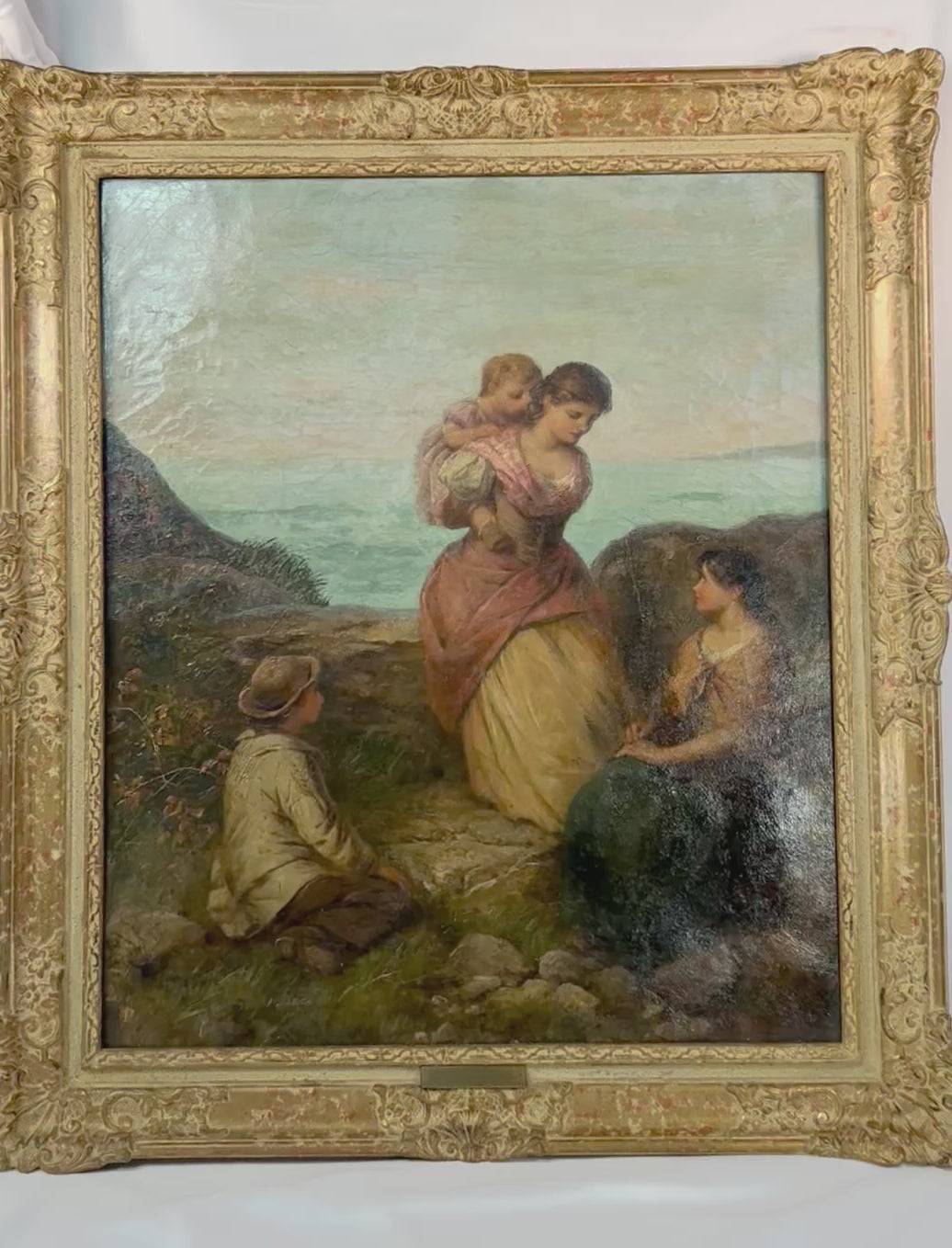 Victorian oil painting “Happy Moments” by Edward John Cobbett R.B.A., depicting a mother holding her child with figures in a rural coastal setting, framed in ornate gilt gesso, England, circa 1860–1880.