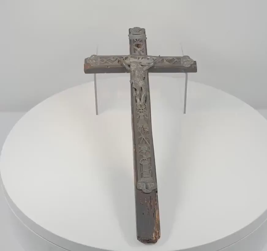 360-degree rotating view of an antique 18th-century French peddler’s crucifix featuring an embossed lead Corpus Christi figure, intricate Arma Christi Passion symbols, decorative religious motifs, and a dark-painted pine wooden cross. Shows the detailed metalwork, aged surfaces, and original hanging loop on the reverse.