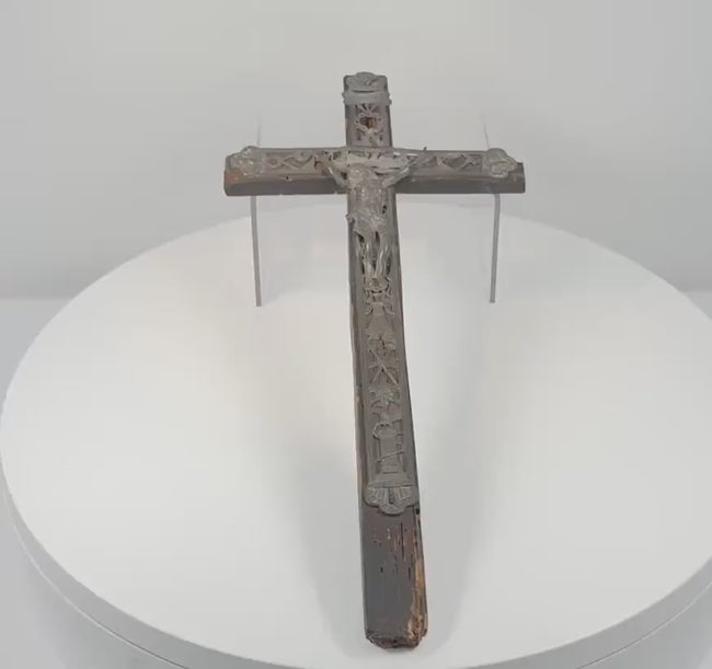 360-degree rotating view of an antique 18th-century French peddler’s crucifix featuring an embossed lead Corpus Christi figure, intricate Arma Christi Passion symbols, decorative religious motifs, and a dark-painted pine wooden cross. Shows the detailed metalwork, aged surfaces, and original hanging loop on the reverse.