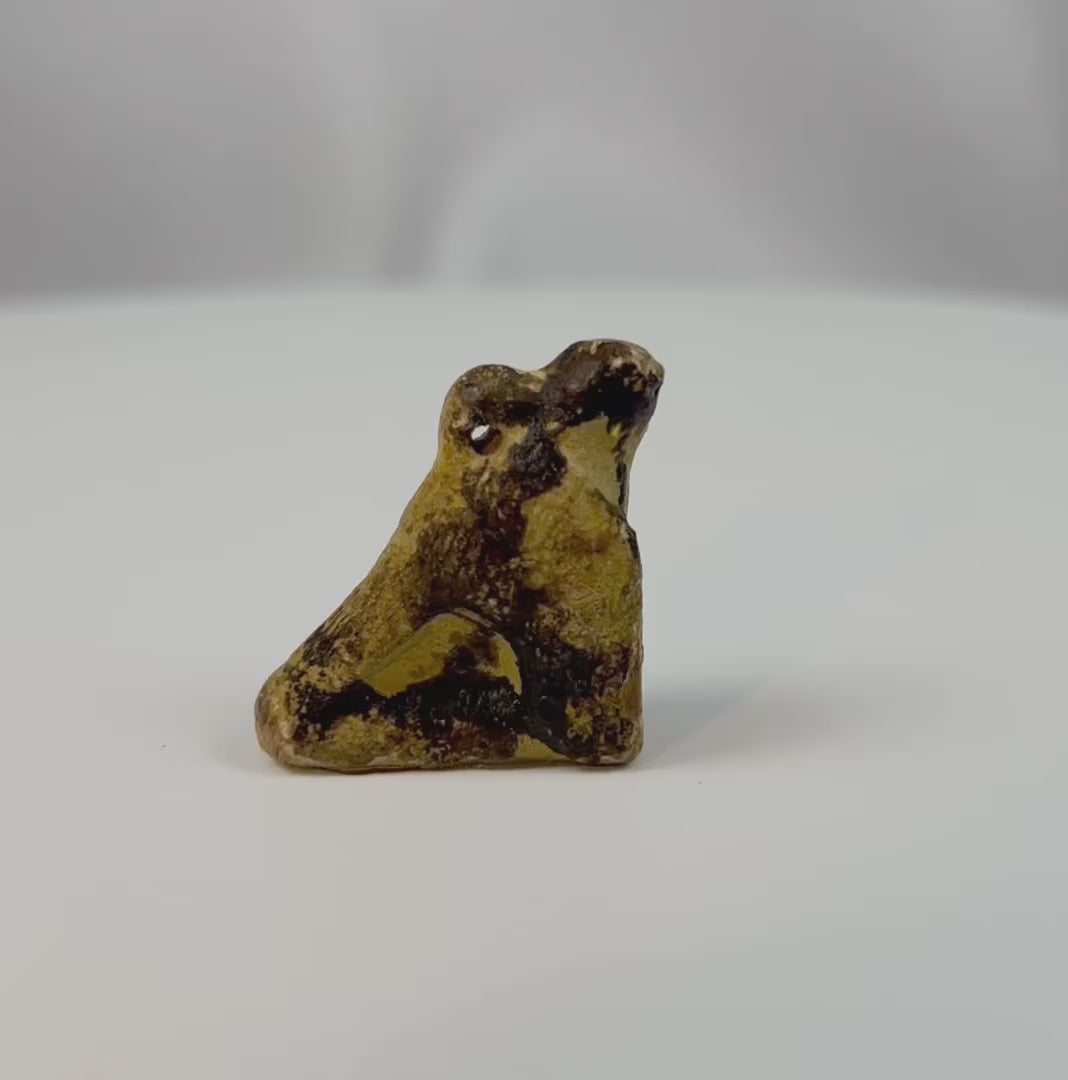 360-degree view of an ancient Egyptian carved stone falcon amulet associated with the god Horus, showing the crouching form and natural mineral patina from the Late Period.