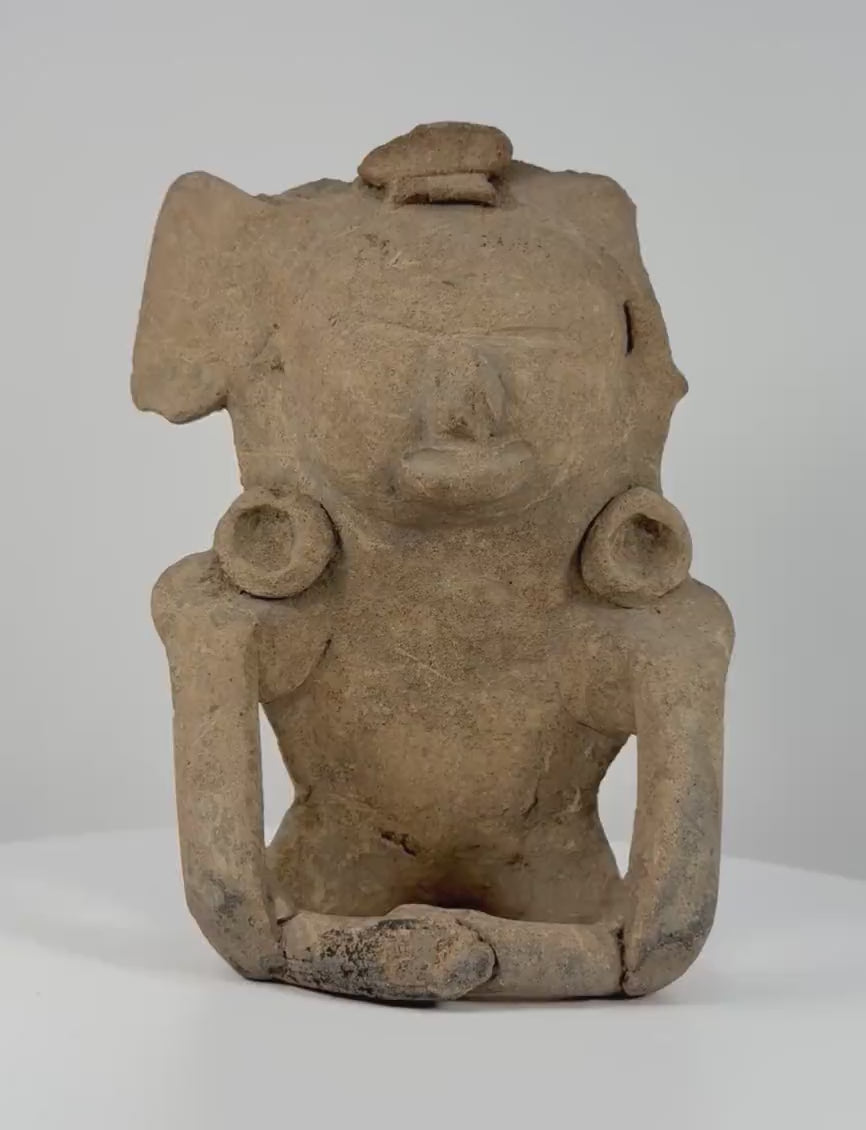 360-degree rotating view of a Pre-Columbian seated terracotta ceramic human figure with a ritual headpiece, sculpted facial features, circular ear ornaments, and bent arms, dating to circa 200–800 CE.