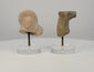 360-degree rotating view of two ancient terracotta artifacts: a Roman female bust featuring an elaborate Flavian-style curled hairstyle and detailed facial features, alongside a Mesopotamian bovine protome depicting a stylized bull's head and neck. Both fragments display weathered surfaces, age-related wear, and distinctive craftsmanship, presented on individual clear acrylic display stands.