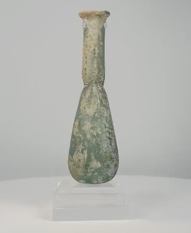 360-degree rotating view of an ancient Roman green glass unguentarium perfume bottle, circa 1st–4th century CE, featuring a pear-shaped body, elongated cylindrical neck, flared rim, and extensive earthy mineral encrustations across its olive-green glass surface.