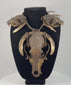 Video of an animal skull necklace on a black display bust, featuring a large central skull, two smaller skulls, curved teeth, and woven twine.