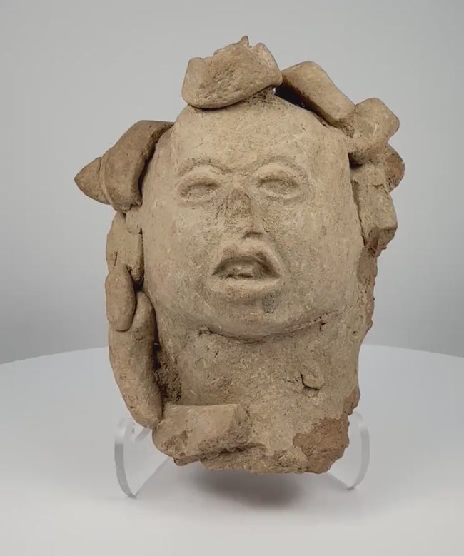 Video showcasing an ancient Pre-Columbian Mesoamerican terracotta head dating to circa 1000–1500 CE, highlighting its elaborate headdress, half-closed eyes, slightly open mouth, hand-formed clay construction, and naturally aged earthen patina.