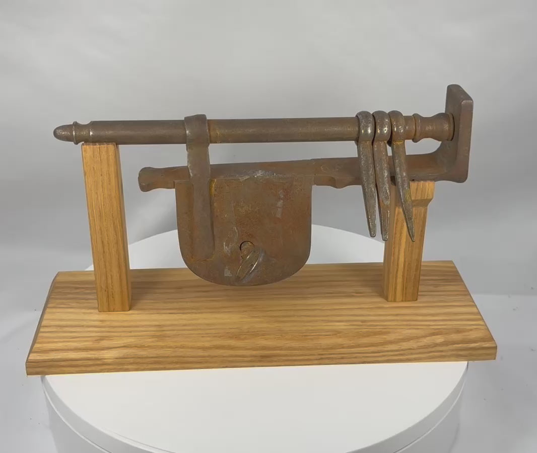 Rotating presentation of an antique European wrought-iron sliding hasp gate lock with key, mounting staples, and custom display stand