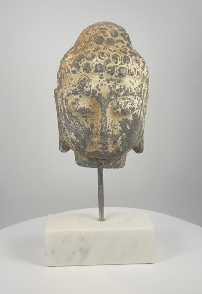 Video showing multiple angles of an 18th–19th century Southeast Asian carved stone Buddha head with curled hair, traces of pigment and a modern marble display base