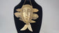 Mid-20th-century Lega tribal pendant mask from the Congo, carved bone face with braided fiber collar, wood backing, and hanging cord, displayed on a black stand against a white background.