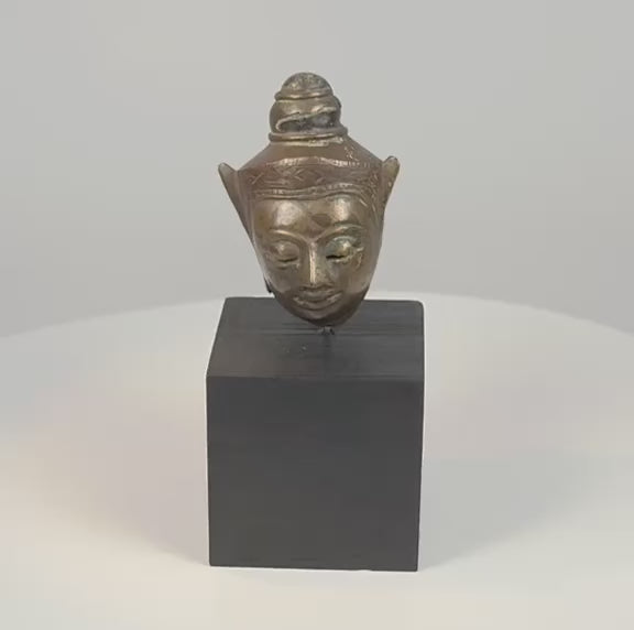 360-degree video of an 18th–19th century Southeast Asian crowned metal Buddha head, showing its serene facial features, aged patina, decorative crown, and black wooden display base