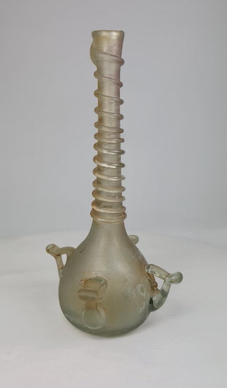 360° video of an antique Islamic blown-glass bottle featuring a spiral-threaded neck and applied handles, circa 12th–14th century CE, displayed on a neutral background.