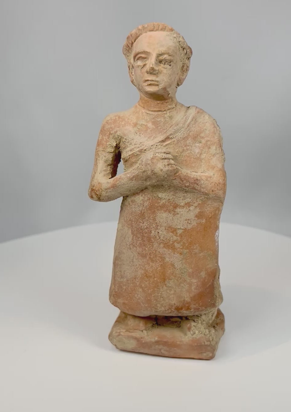 Rotating view of primitive terracotta standing male figure with textured surface and stylized features