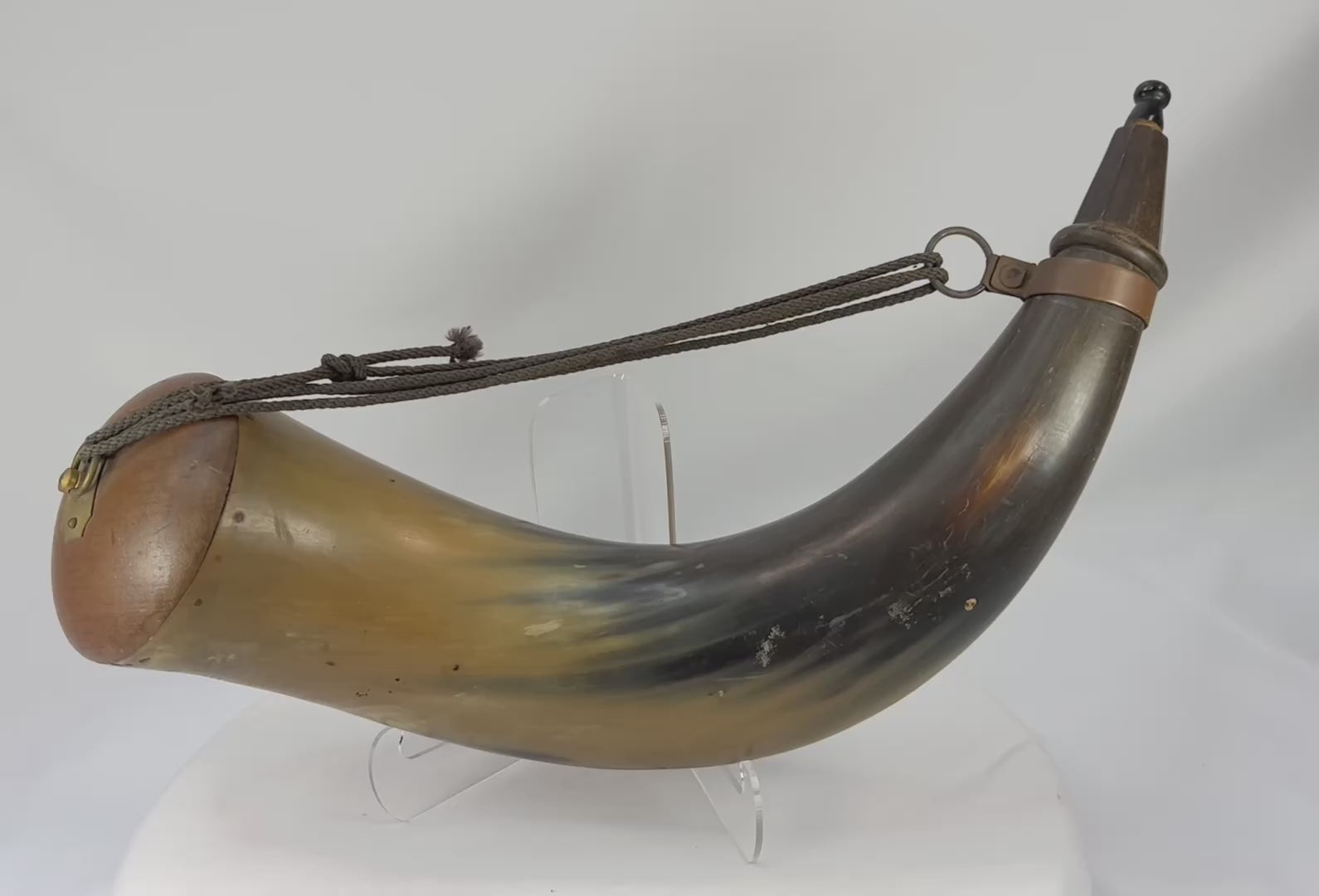 60-degree rotating view of an antique black powder horn from circa 1780–1830, showing polished horn body, wooden fittings, brass mount, and attached carry cord.