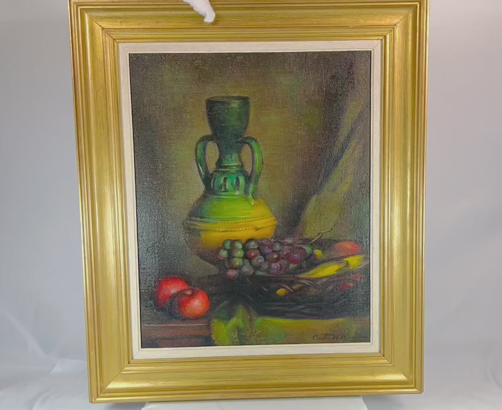 Mid-20th century still life oil painting depicting a green vase, grapes, and apples on a tabletop. Signed by the artist, framed in a gilded wooden frame, with rich colors and detailed brushwork.