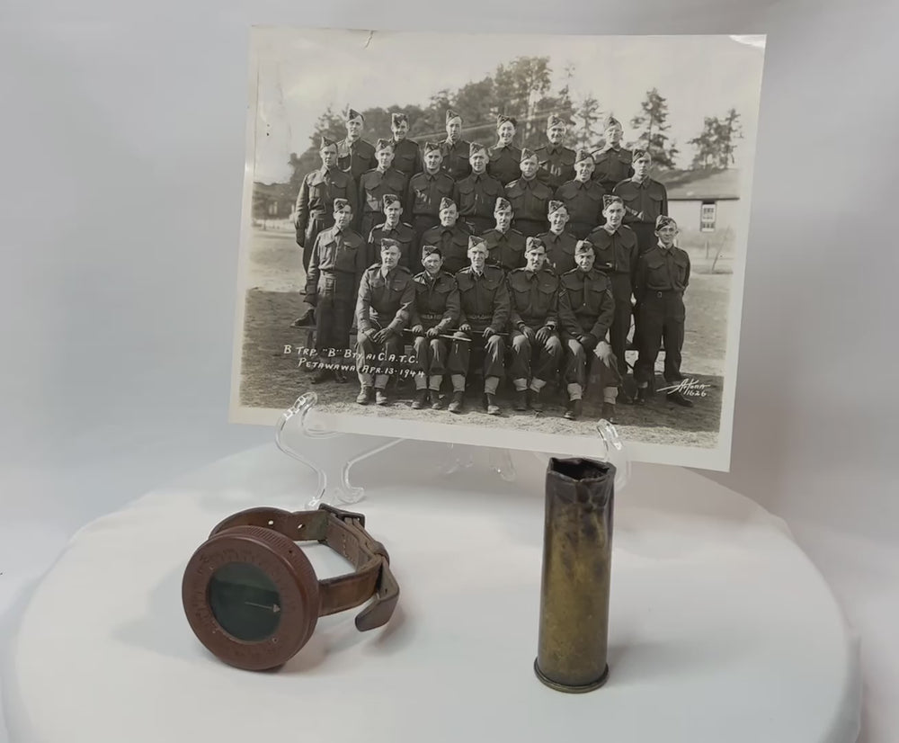Vintage WWI military memorabilia set including a soldier’s wrist compass, a spent shell casing, and a sepia-toned unit photograph of troops, displayed on a white background.