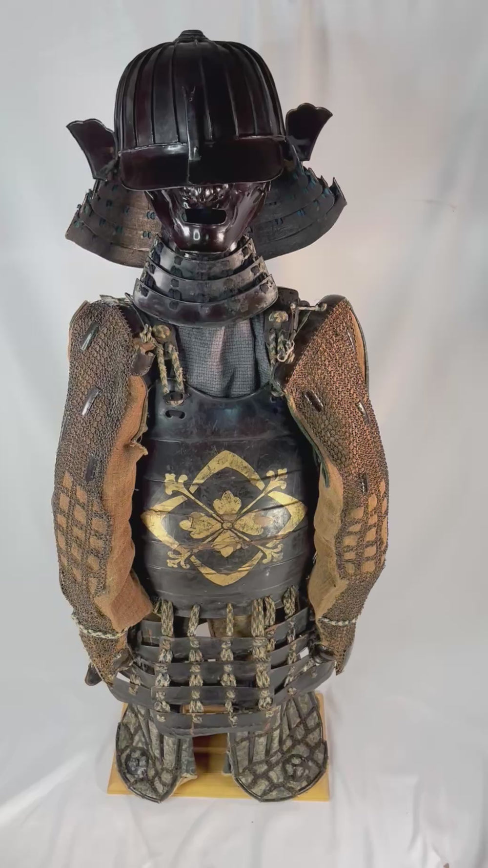 Authentic Japanese samurai armor set from the Muromachi Period (1333–1573), featuring a black-lacquered 24-plate suji-bachi kabuto helmet, menpo facial armor, gold-painted mon on the cuirass, Edo-period silk lacing, and chainmail sleeves, displayed on a wooden stand against a white background