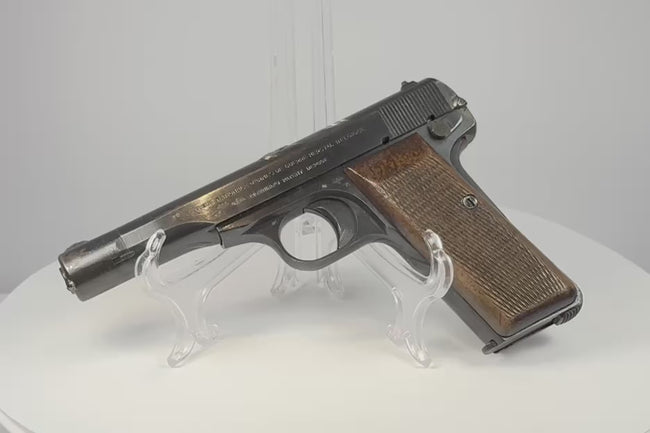 Video of a deactivated WWII FN Browning Model 1922 on a clear display stand, showing worn blued steel and checkered walnut grips.