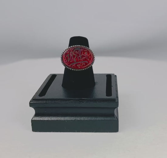 Oval carnelian intaglio ring from the Ancient Near East, 1st millennium BCE. Features engraved animal and symbolic motifs on red carnelian, set in a silver bezel, displayed on a black stand. Excellent condition with finely detailed intaglio carvings.